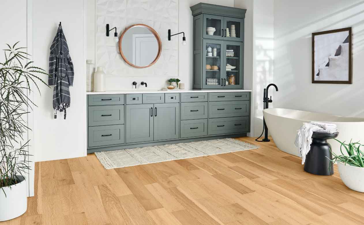 white oak waterproof engineered hardwood in bathroom with deep soak tub and blue cabinetry